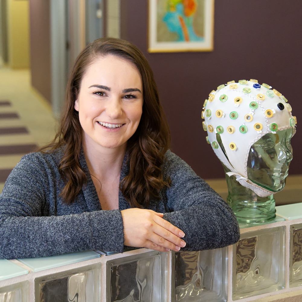 Female research sitting beside white cap on glass mannequin head