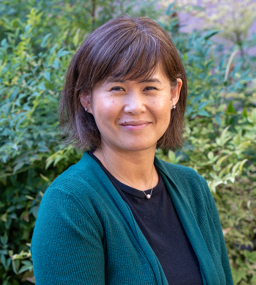 Smiling middle-aged Asian woman with short brown hair in teal cardigan, outdoor portrait