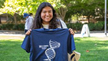 Student smiles while holding up a navy UC Davis College of Biological Sciences T-shirt with a white DNA helix design.