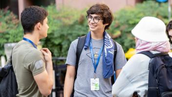 Students wearing UC Davis lanyards chat and smile outdoors during an orientation event on campus.