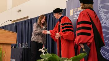 Award recipient shakes hands with a faculty member in academic regalia at a UC Davis stage during recognition ceremony.