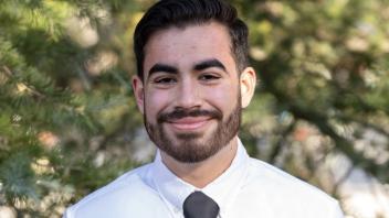 A person with a beard in a white shirt and tie standing outside