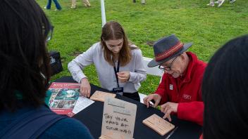 Two individuals demonstrate suturing techniques at a booth labeled "Future Doctor," which invites participants to try their hand at suturing. One participant, dressed in a white shirt, practices sutures while another person in a red sweater assists.