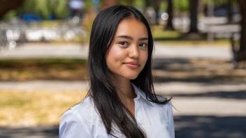 A person standing outside in a white shirt in front of a shaded path
