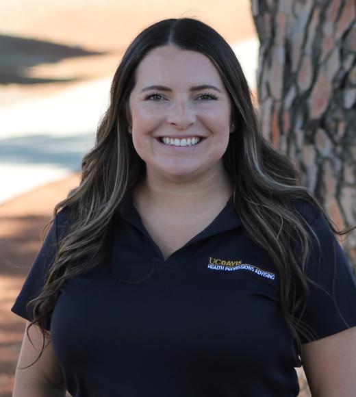 Smiling woman in navy polo with logo, outdoor headshot by a tree