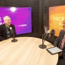 Two men sit at a round table with microphones, smiling and engaging in conversation.
